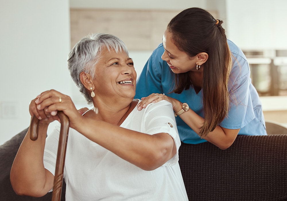 A senior woman smiling at a nurse standing behind her.